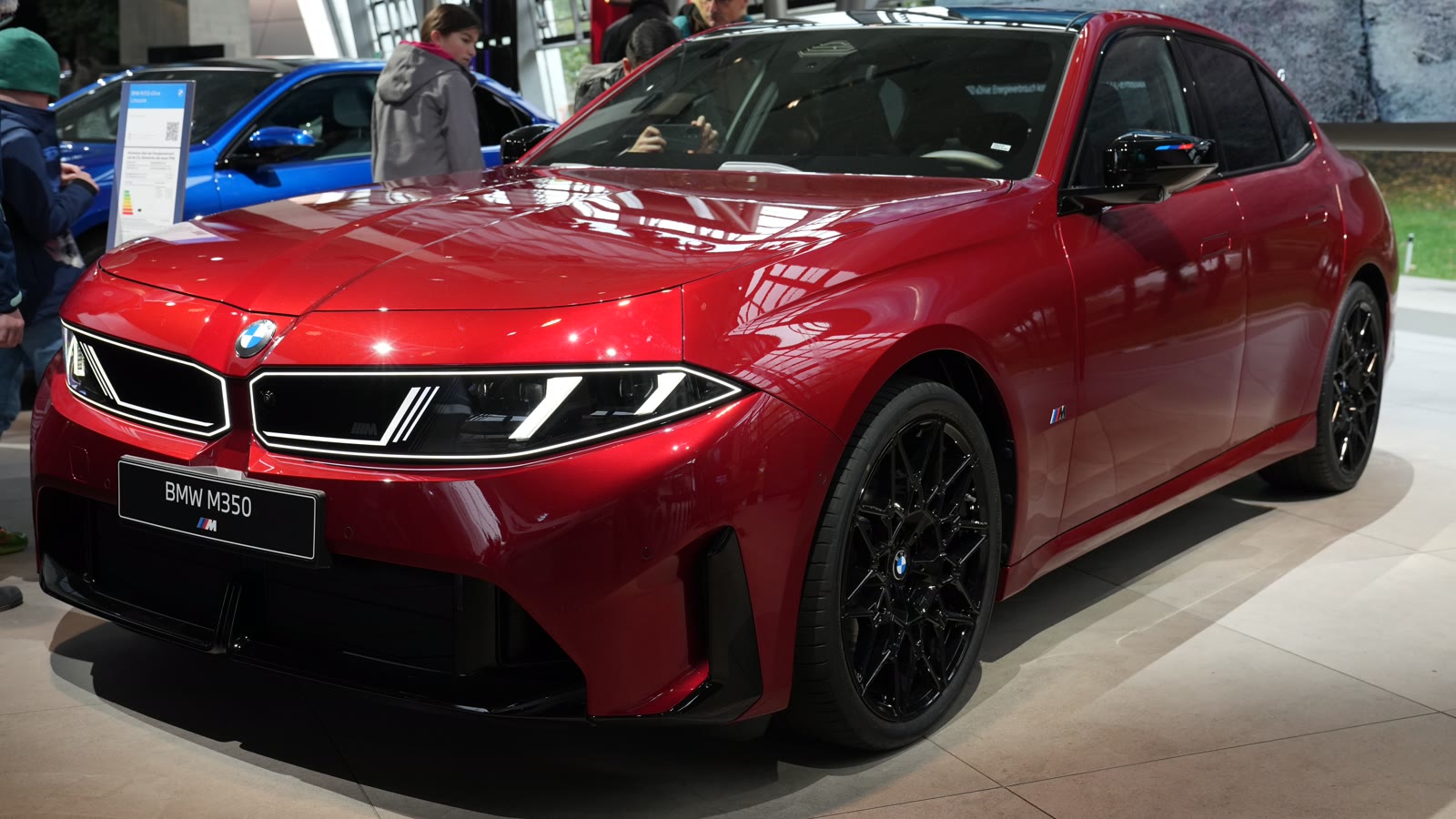 Κόκκινη BMW M350 xDrive Sedan νέας γενιάς σε μπροστινή τριτέταρτη όψη, εκτεθειμένη στο BMW Welt του Μονάχου