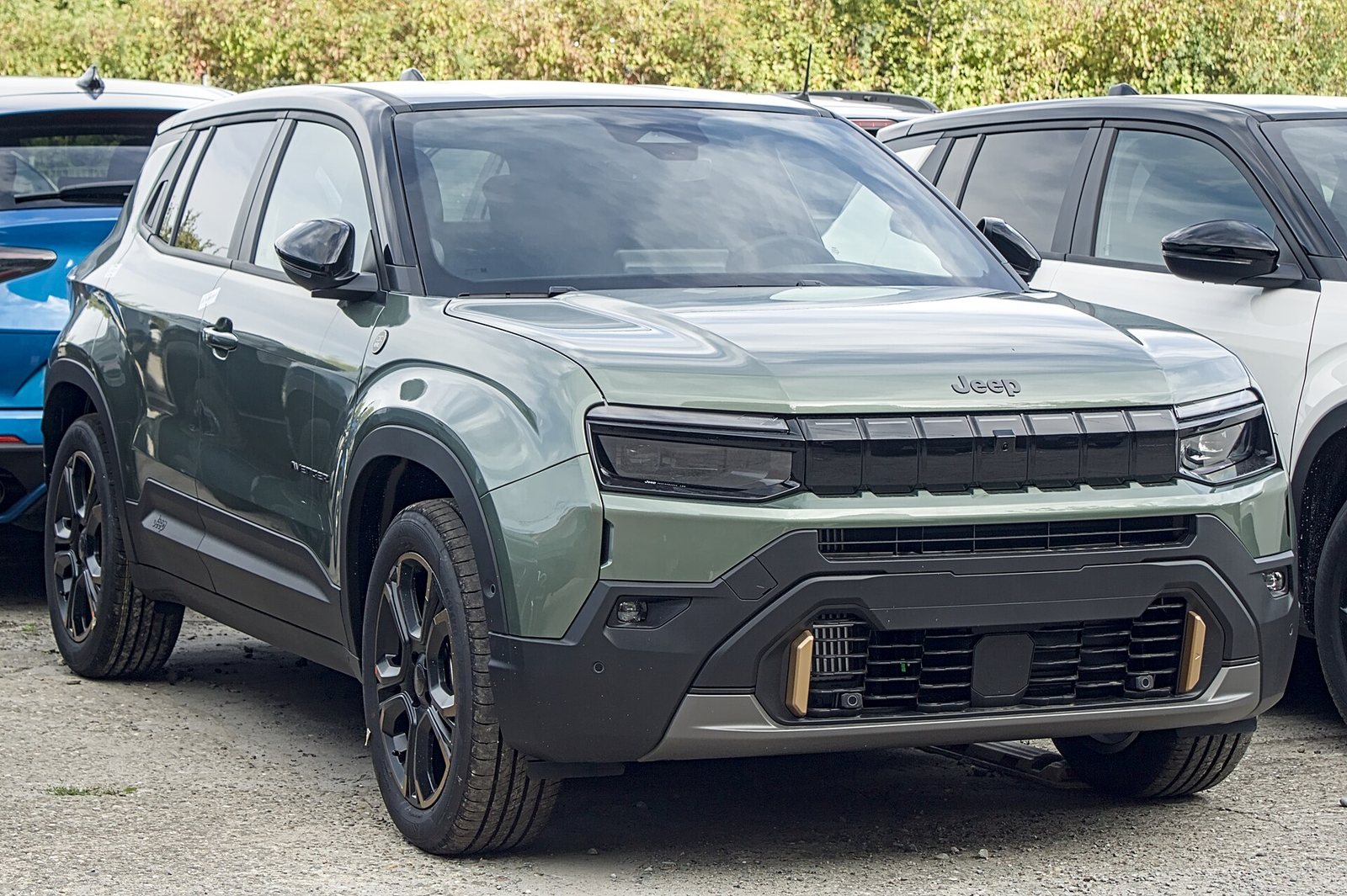 Πράσινο ανανεωμένο Jeep Avenger 85th Anniversary με χρυσές λεπτομέρειες στον προφυλακτήρα, σε μπροστινή τριτέταρτη όψη, σταθμευμένο ανάμεσα σε άλλα αυτοκίνητα